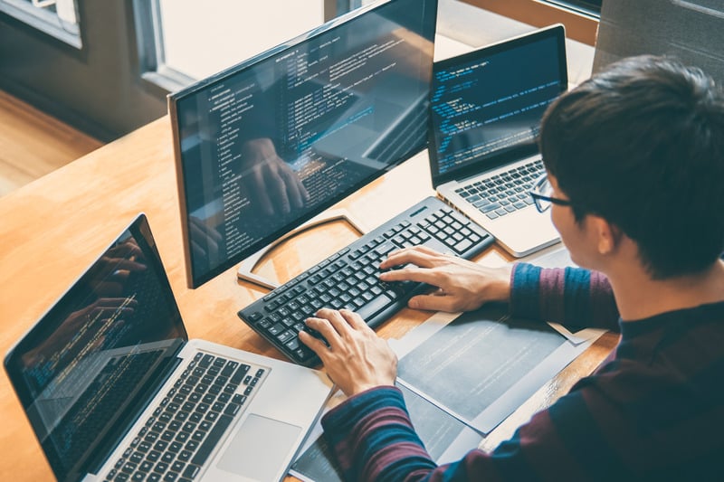 Person coding on multiple computer screens.